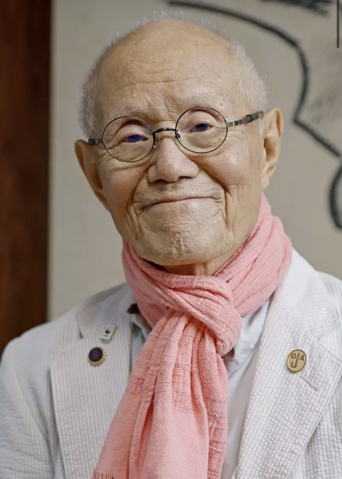Tetsuya Chiba sorrindo, com óculos redondos e cachecol rosa