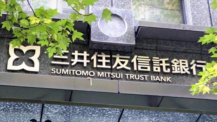 Fachada com o nome e o logotipo do Sumitomo Mitsui Trust Bank entre folhas verdes