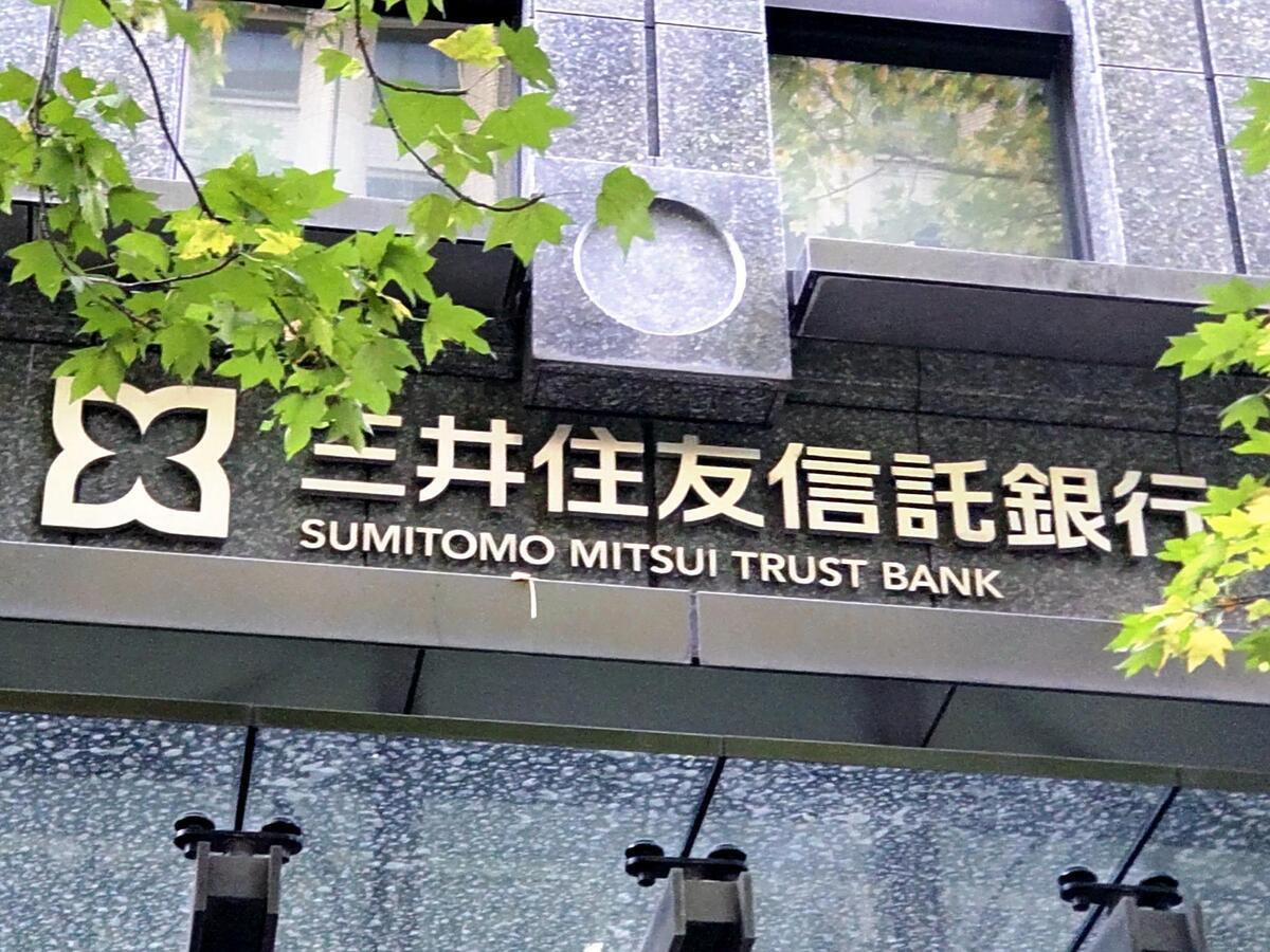 Fachada com o nome e o logotipo do Sumitomo Mitsui Trust Bank entre folhas verdes